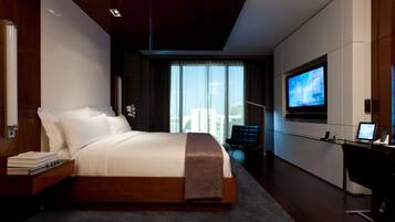 Habitación de hotel moderna con una cama grande, un escritorio con computadora, televisión y vista a la ciudad.
