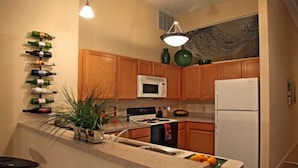 A compact kitchen with wooden cabinets, a white refrigerator, a microwave, and a sink. There is a plant on the counter and a bottle rack on the wall. - Bridgestreet at the Bingham (Cleveland)