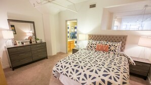 A bedroom with a large bed, a dresser, a mirror, and a nightstand. - Bridgestreet at the Bingham (Cleveland)