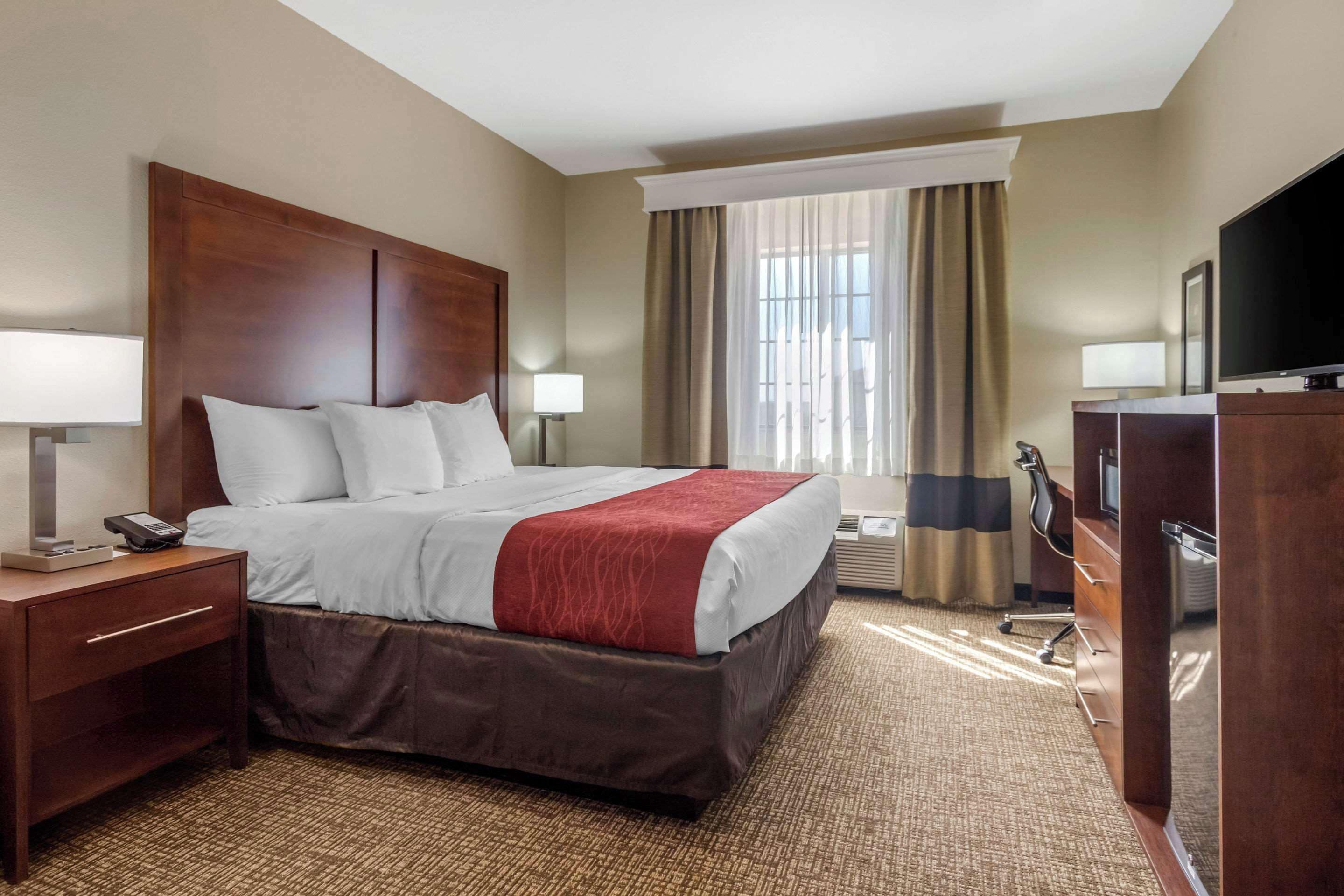 Habitación de hotel con una cama grande, un escritorio con lámpara, televisión y ventana con cortinas.