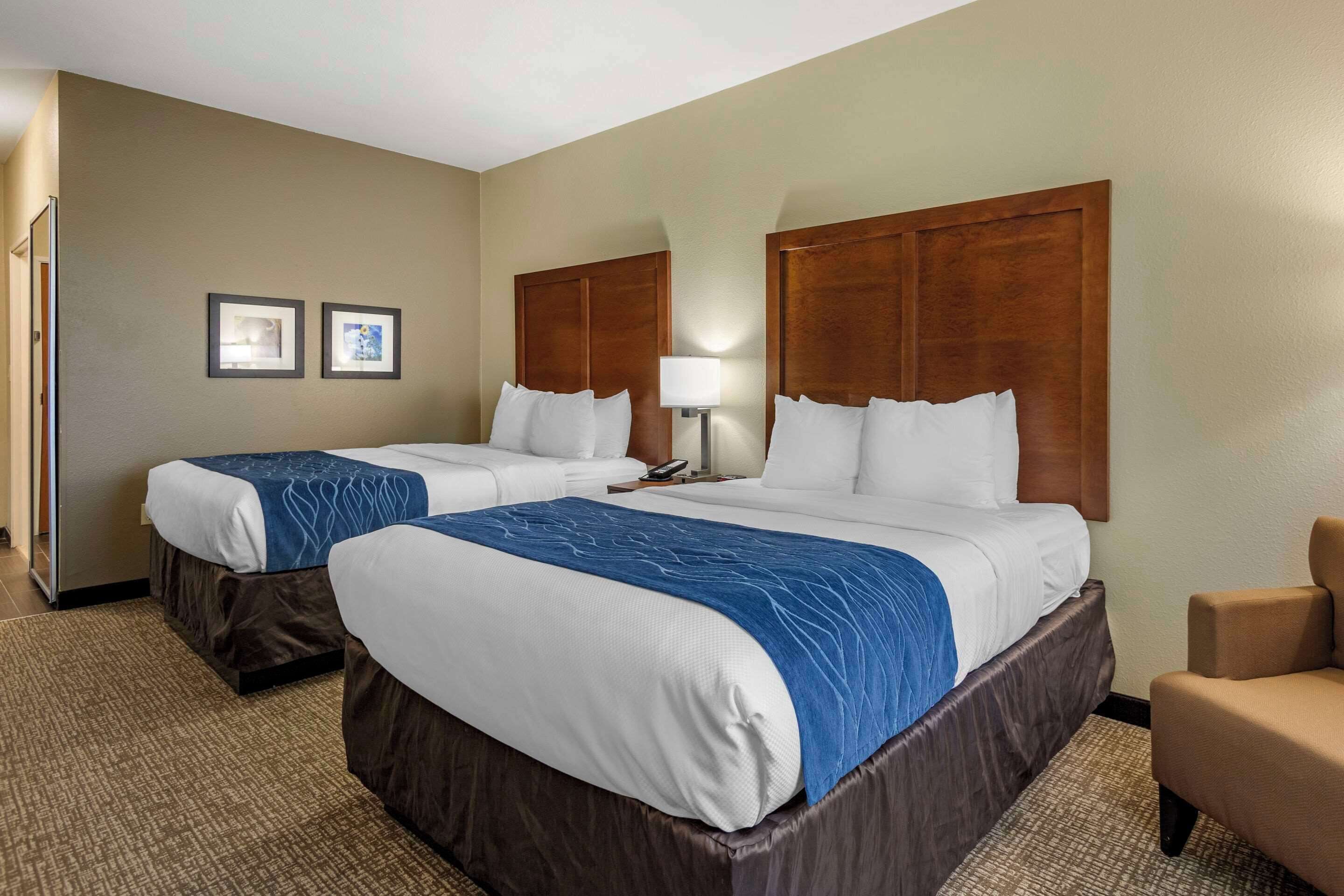 A hotel room with two beds, a desk, a chair, and a lamp.