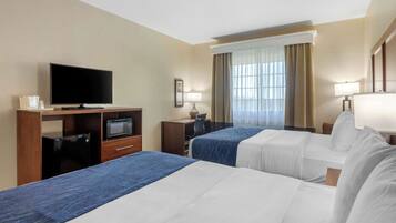 A hotel room with two beds, a television, a desk with a computer, and a window with curtains.
