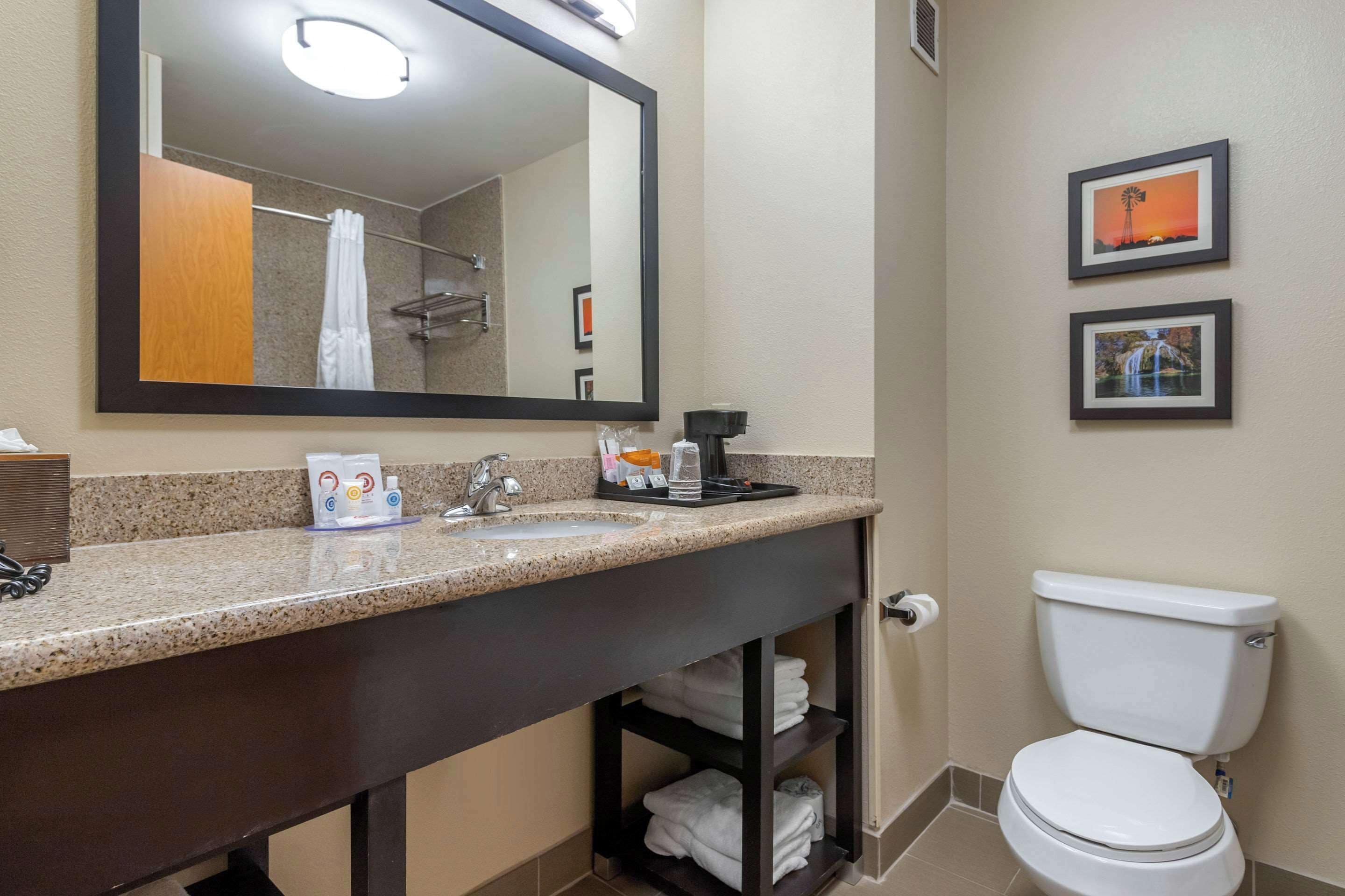 A bathroom with a sink, mirror, toilet, and two framed pictures on the wall.