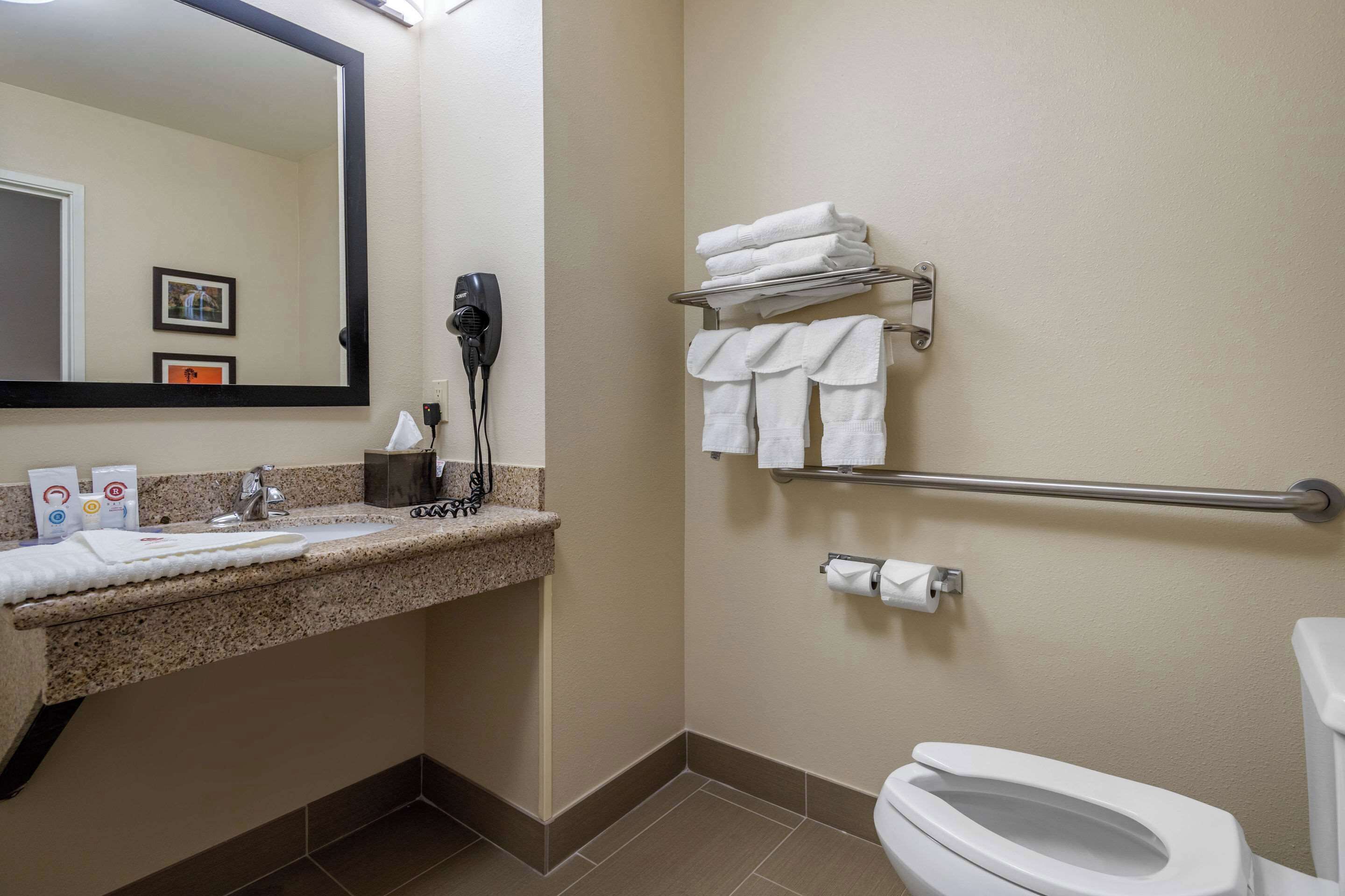 A bathroom with a sink, mirror, towel rack, toilet, and a hairdryer.