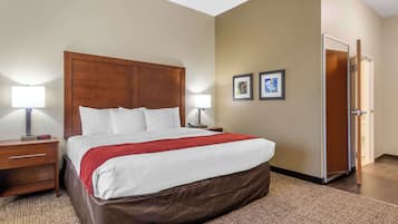 A hotel room with a large bed, two bedside tables, a nightstand, a red throw blanket, and two framed pictures on the wall.