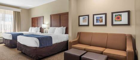 A hotel room with two beds, a brown sofa, and three framed pictures on the wall.