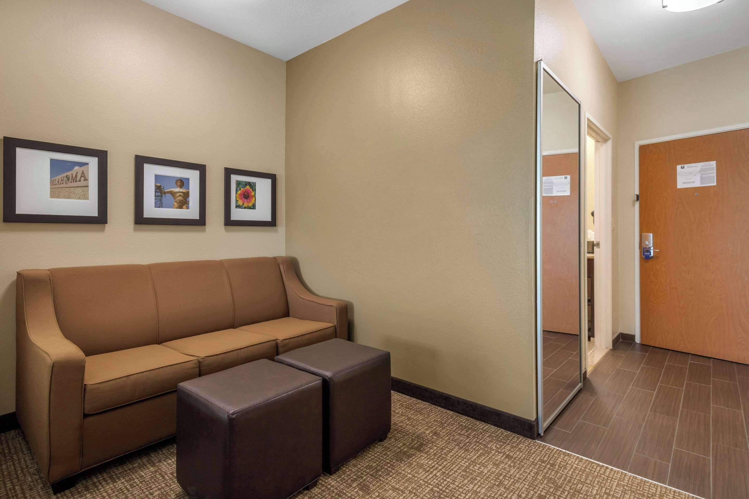 Un hall de hotel con una pared color beige, un sofá marrón, dos otomanas y tres cuadros enmarcados.