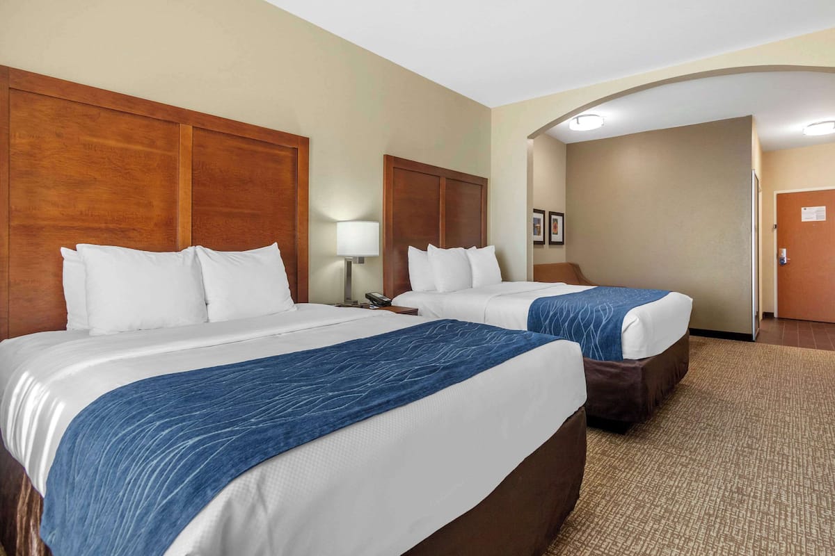 A hotel room with two beds, wooden headboards, and a carpeted floor.