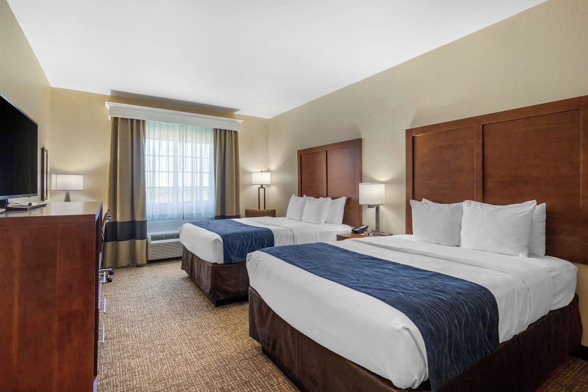 A hotel room with two beds, a desk, a TV, and a window with curtains.