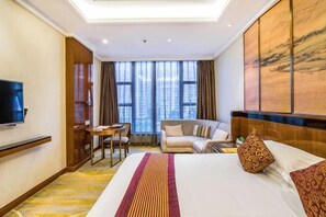 A hotel room with a bed, a television, a seating area with a table and chairs, and large windows. - Yuntianlou Milan International Hotel (Wenzhou)