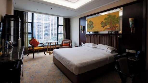 A hotel room with a large bed, a desk, a chair, a TV, and a window with a city view. - Yuntianlou Milan International Hotel (Wenzhou)