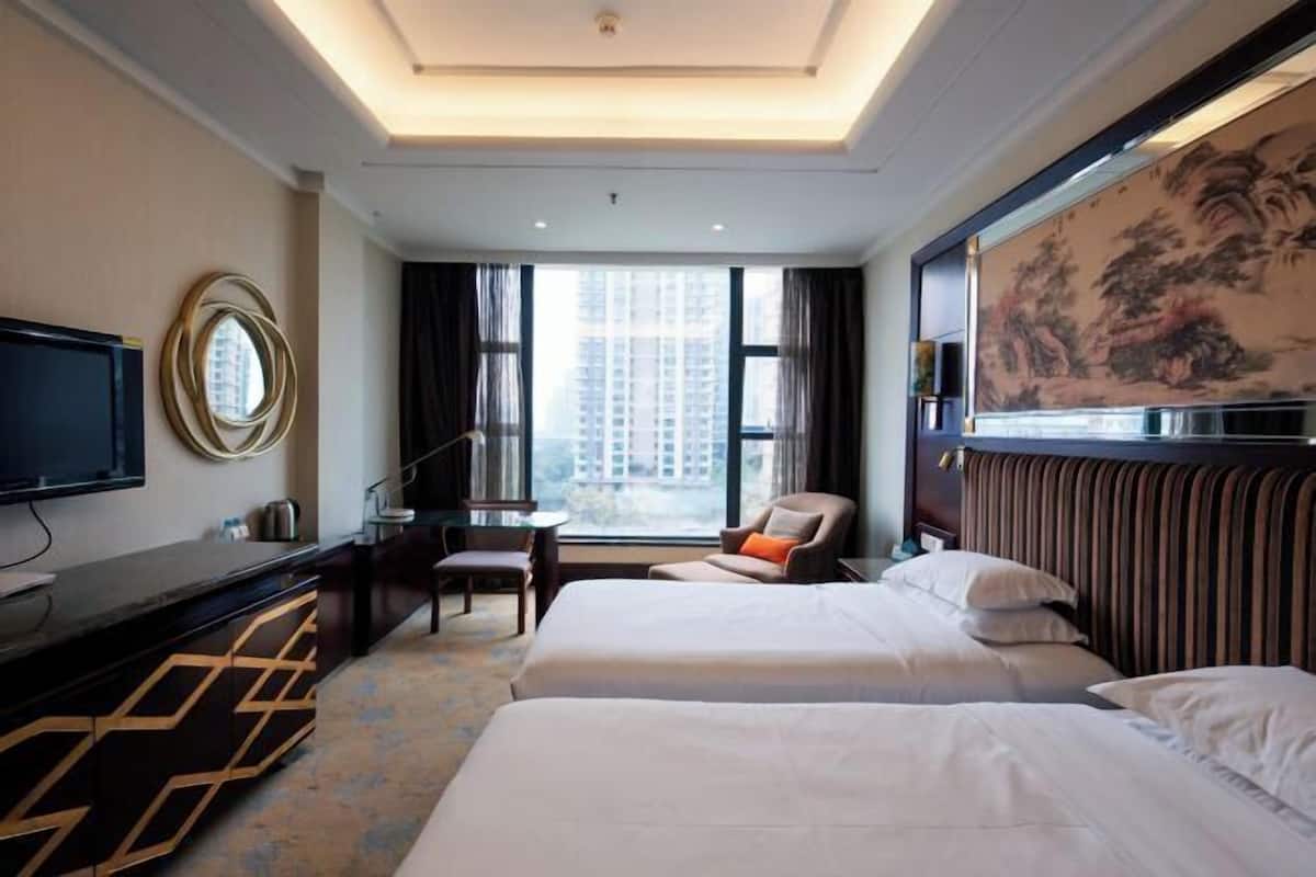 A hotel room with two beds, a desk, a chair, a TV, and a large window.