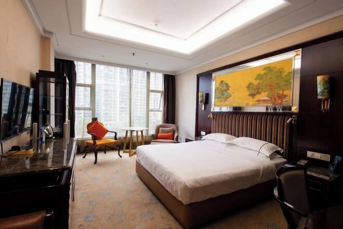 A hotel room with a large bed, a desk, a chair, a TV, and a painting on the wall.