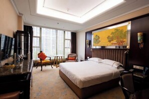 Een hotelkamer met een groot bed, een bureau, een stoel, een televisie en een schilderij aan de muur.