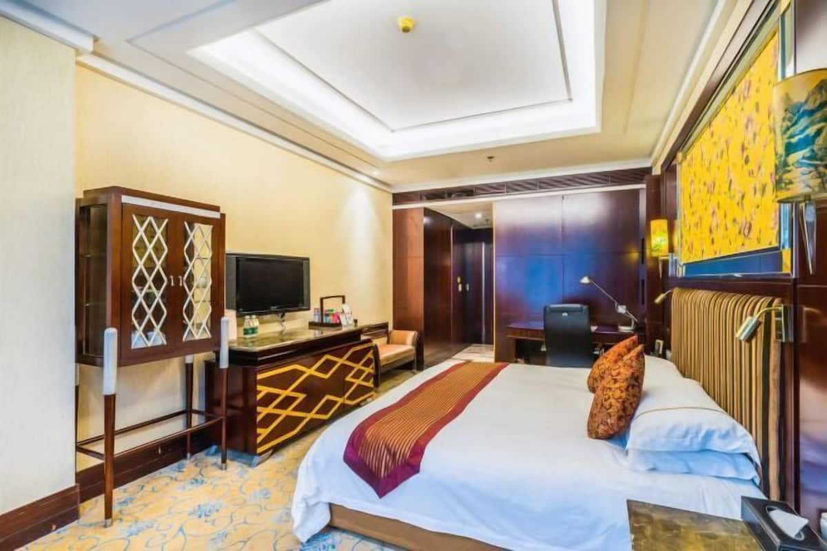 A hotel room with a bed, desk, television, and a view of the outside.
