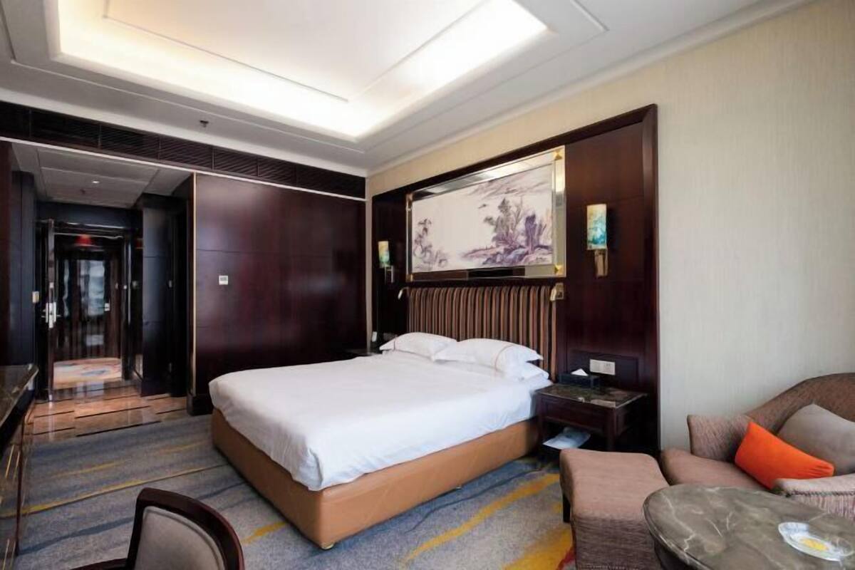 A hotel room with a large bed, a desk, a chair, and a small table.