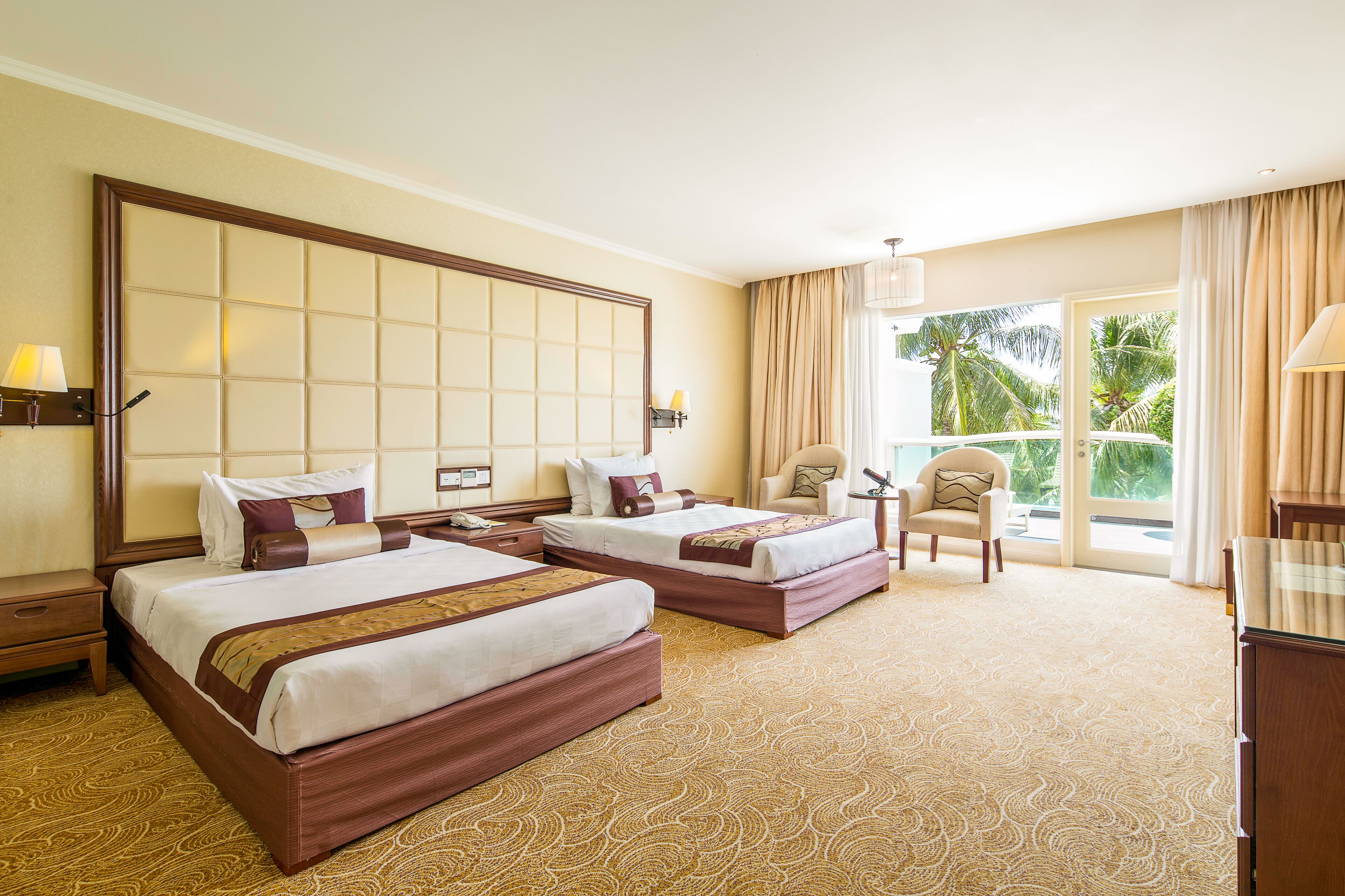 A hotel room with two beds, a sitting area, and a balcony with a view.