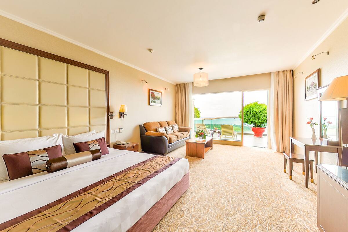 Een hotelkamer met een groot bed, een bank, een eettafel en een balkon met uitzicht.