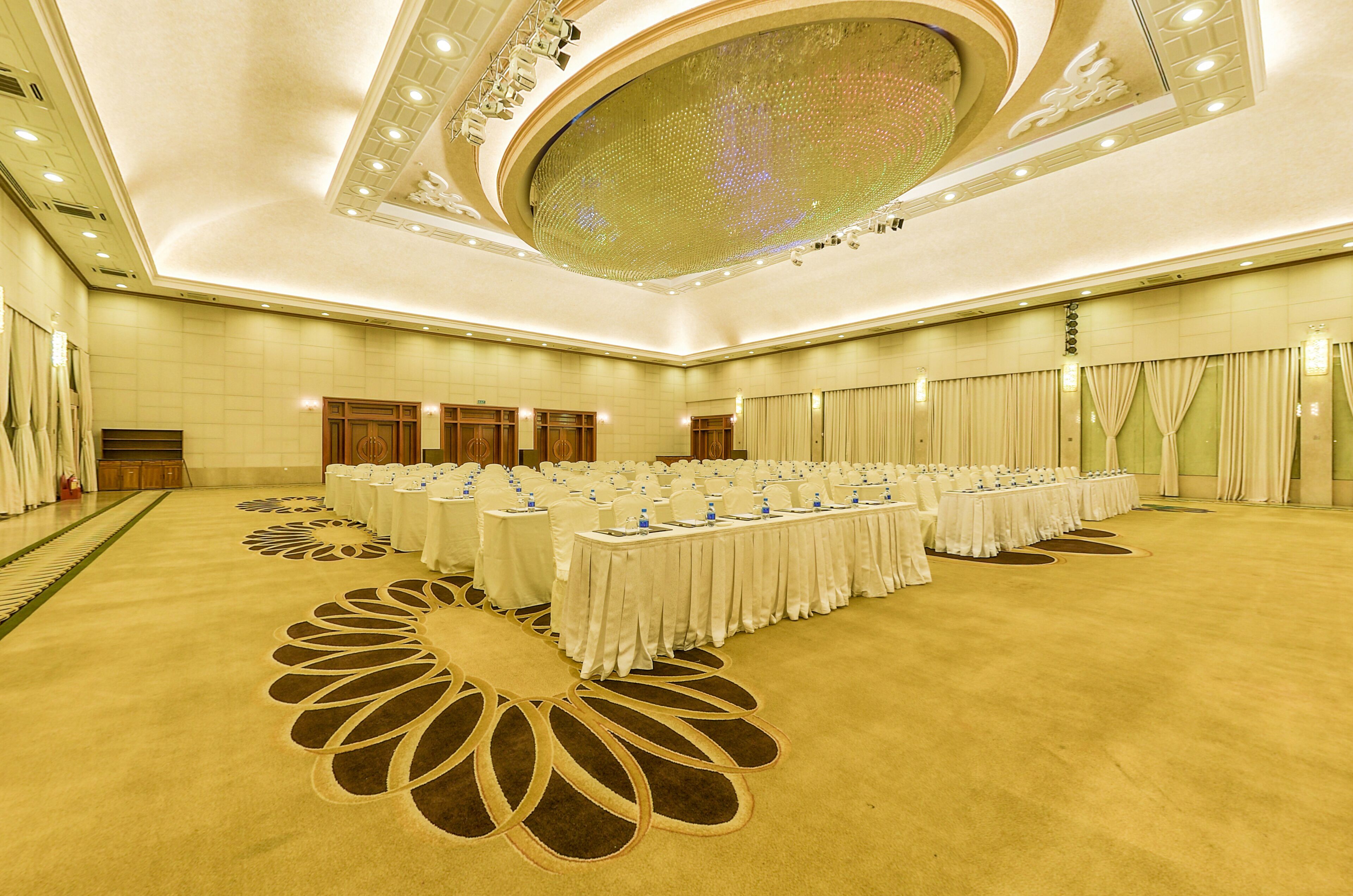A large banquet hall with long tables set for events, a decorative ceiling, and a carpet with a floral pattern.