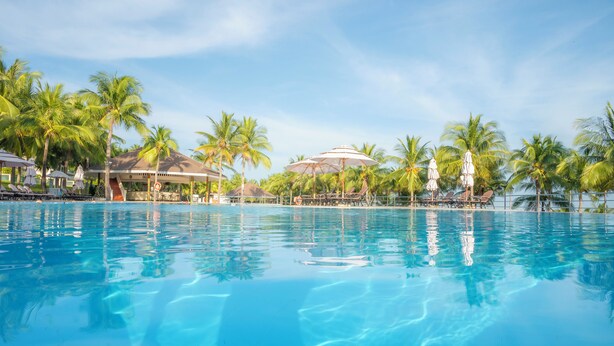A clear blue pool surrounded by palm trees and lounge chairs, with a covered seating area in the background. - Sea Links Beach Hotel (Phu Thuy)