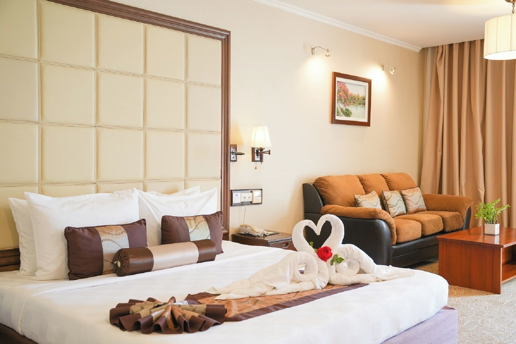 A hotel room with a bed, a sofa, a nightstand, a lamp, and a painting on the wall.