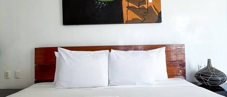 Une chambre d’hôtel avec un grand lit, du linge de lit blanc, deux oreillers blancs et un tableau décoratif au-dessus du lit.