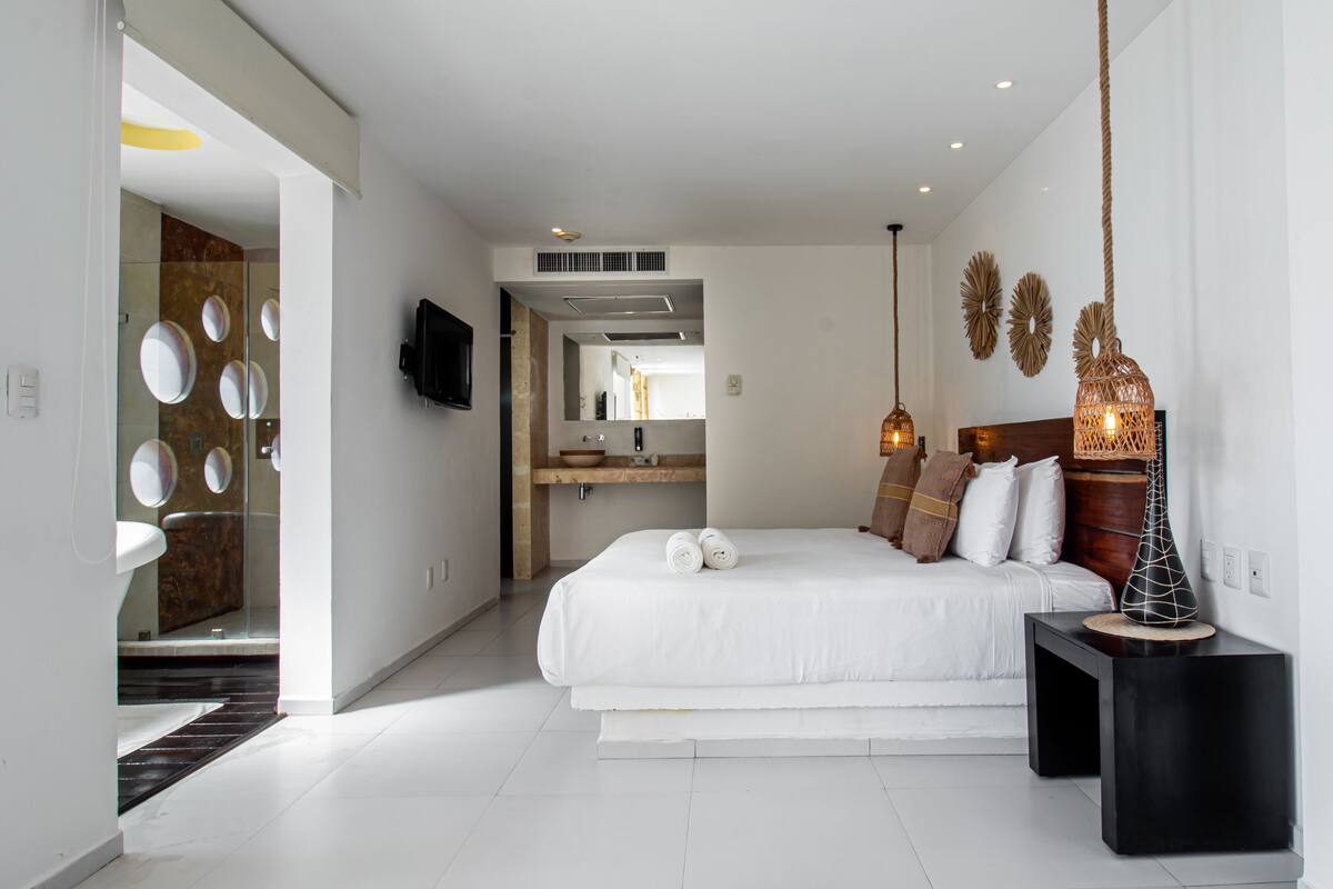 Une chambre d’hôtel moderne dotée d’un grand lit, d’un téléviseur fixé au mur et d’un miroir rond au design original qui décore le mur.