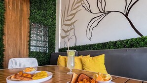 A dining area with wooden tables, a green wall with foliage, and a wall art of leaves. - Cache Hotel Boutique - Adults Only (Playa del Carmen)