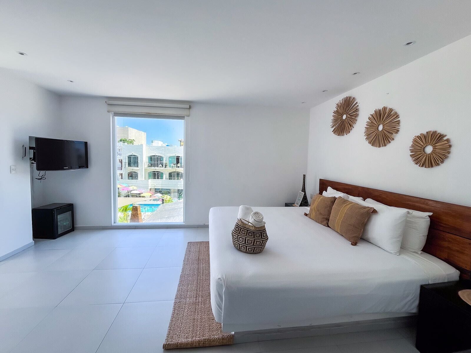 Ein modernes Schlafzimmer mit einem großen Bett, einem Flachbildfernseher und Blick auf einen Pool sowie Gebäude.