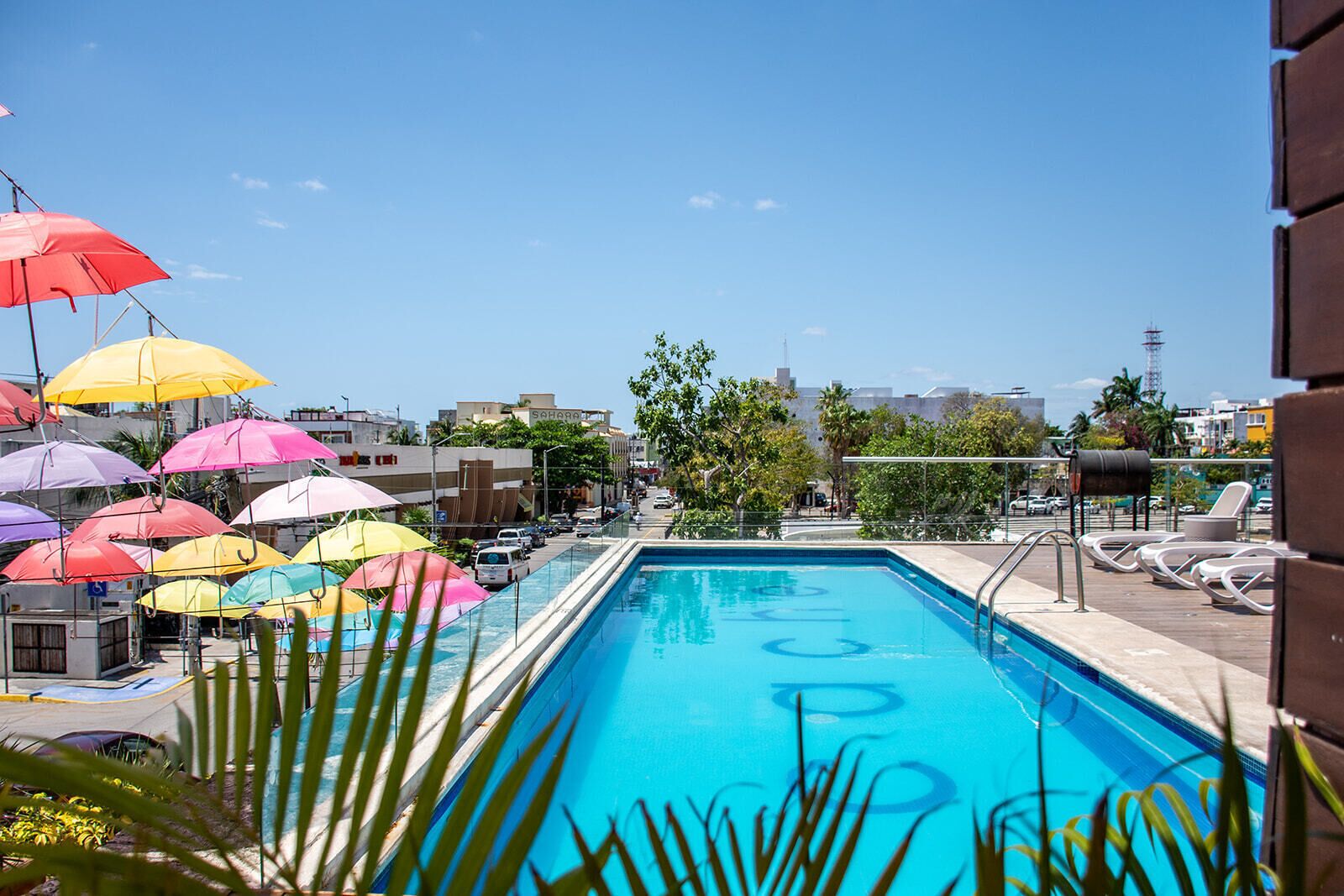 Una piscina con sombrillas de colores, sillas de descanso y vistas a la ciudad.