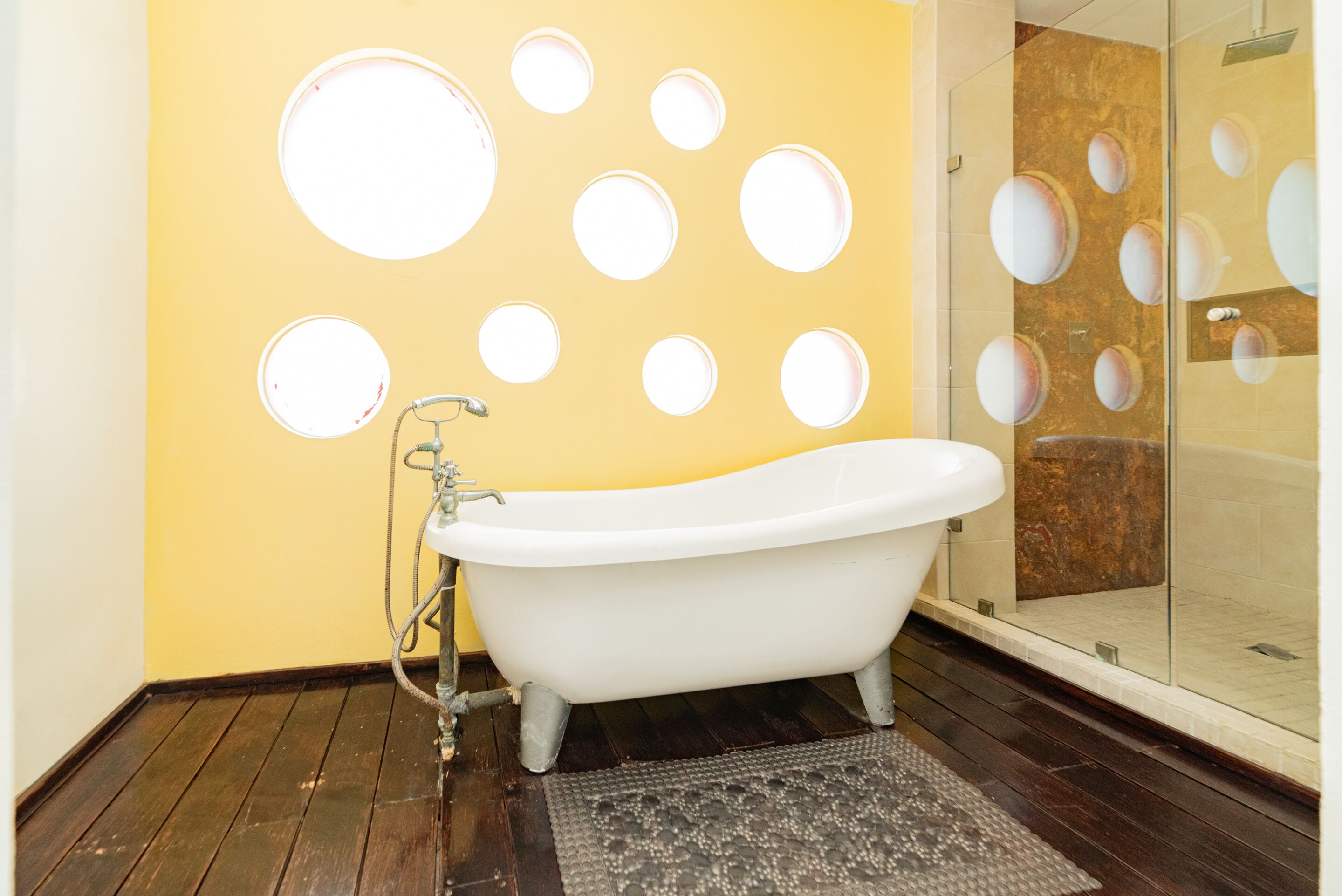 Un baño con una bañera blanca tipo pata de león, cabina de ducha de cristal y una pared con abertura circulares.