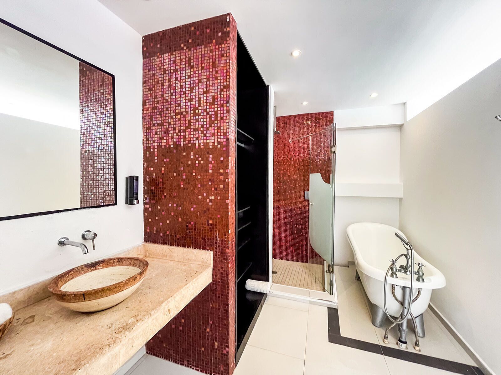 A modern bathroom with a mosaic tile wall, a wooden bowl sink, and a vintage-style bathtub.