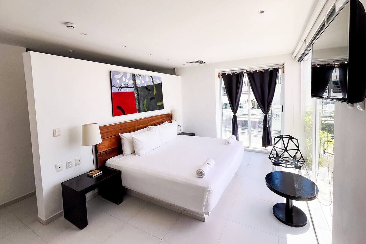 Une chambre d’hôtel moderne dotée d’un grand lit, d’un téléviseur à écran plat, d’une petite table et d’une fenêtre avec des rideaux.