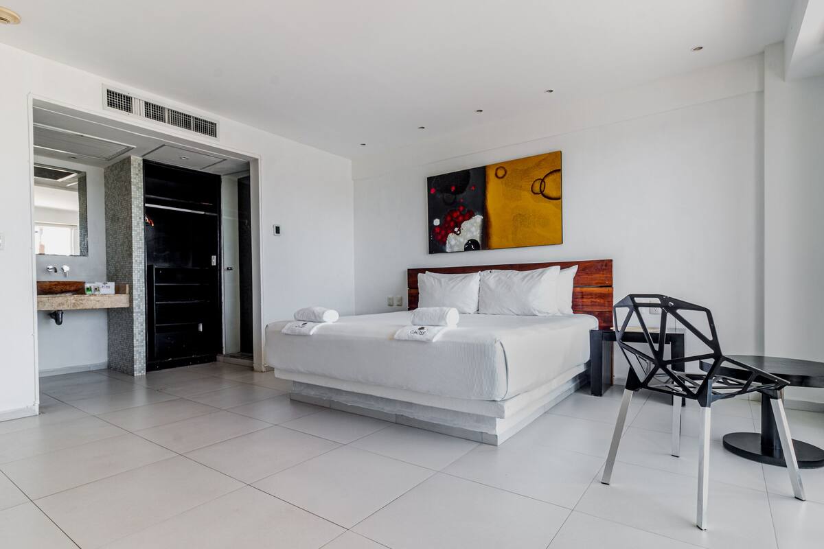 Une chambre d’hôtel moderne avec un grand lit, une table de chevet, une chaise et un tableau au mur.