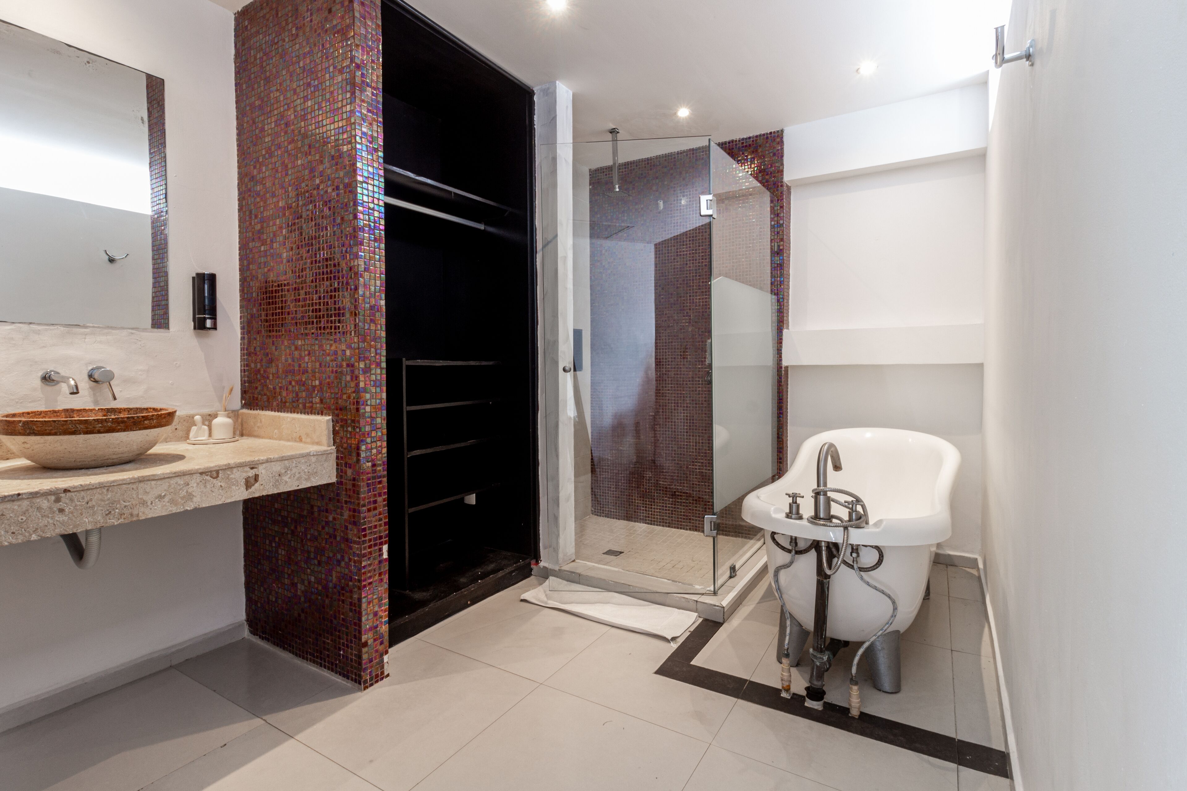 A modern bathroom with a large mirror, a bowl sink, a glass-enclosed shower, and a white pedestal sink.