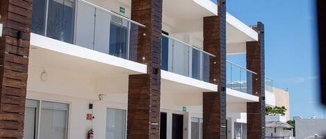 A modern building with a white facade, multiple balconies, and a pool area with lounge chairs.