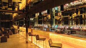 Una zona de bar con una barra alargada, varios taburetes y una amplia selección de botellas y vasos a la vista.