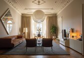 A spacious living room with a large sofa, two armchairs, a dining table, and a TV.