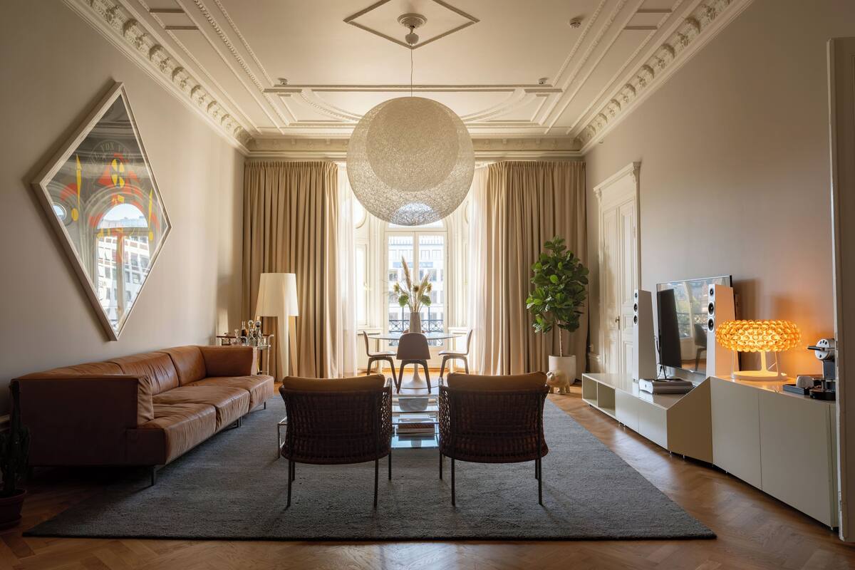 A spacious living room with a large sofa, two armchairs, a dining table, and a TV.