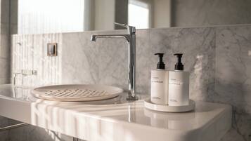 Un baño moderno con lavamanos de mármol blanco, un grifo cromado y dos botellas de crema corporal Fredi.