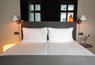 A neatly made bed with white linens, two bedside lamps, and a small table with a vase of flowers.