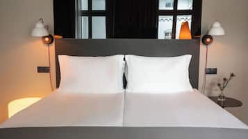 A neatly made bed with white linens, two bedside lamps, and a small table with a vase of flowers.