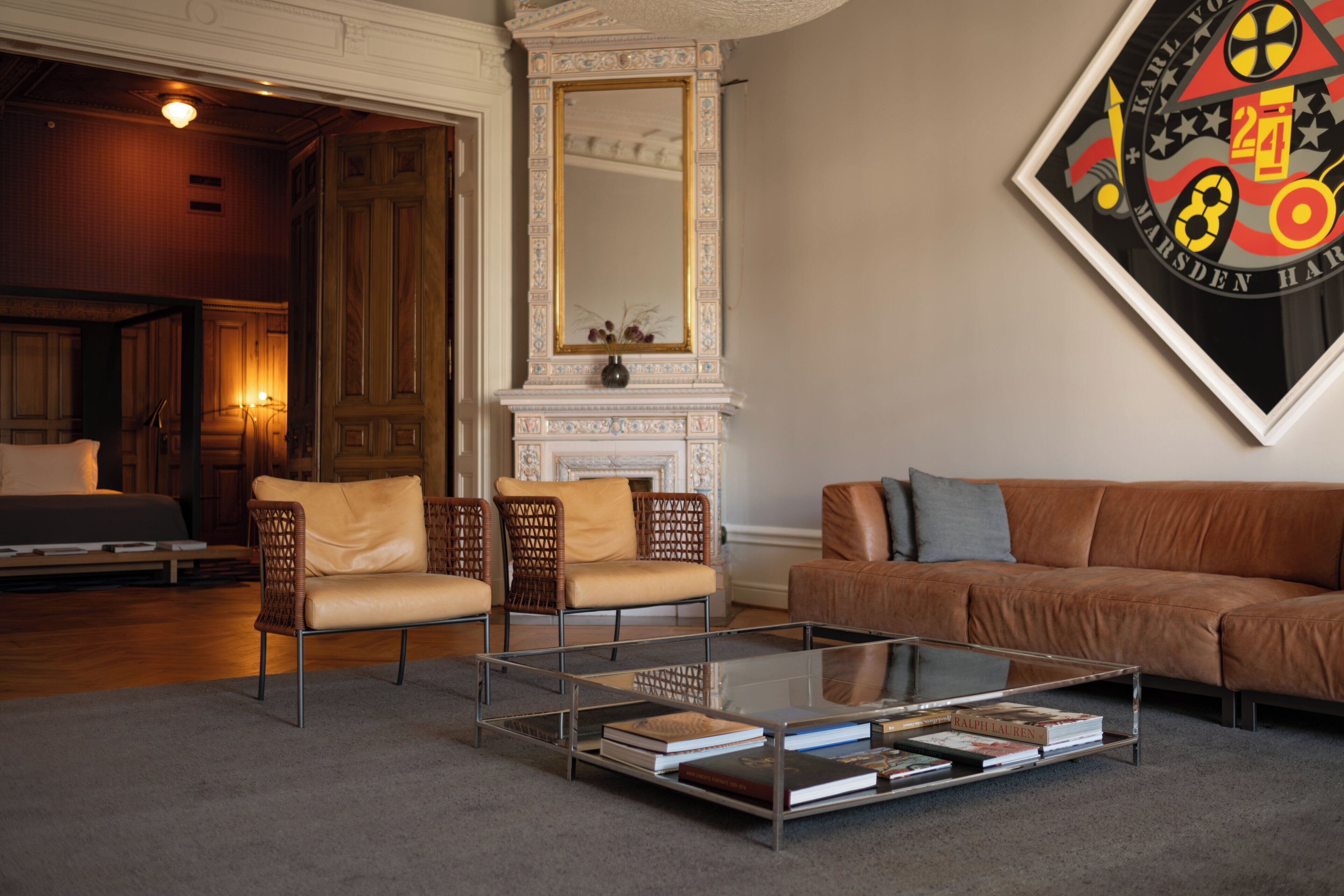 A modern living room with a glass coffee table, leather sofa, and wicker chairs.