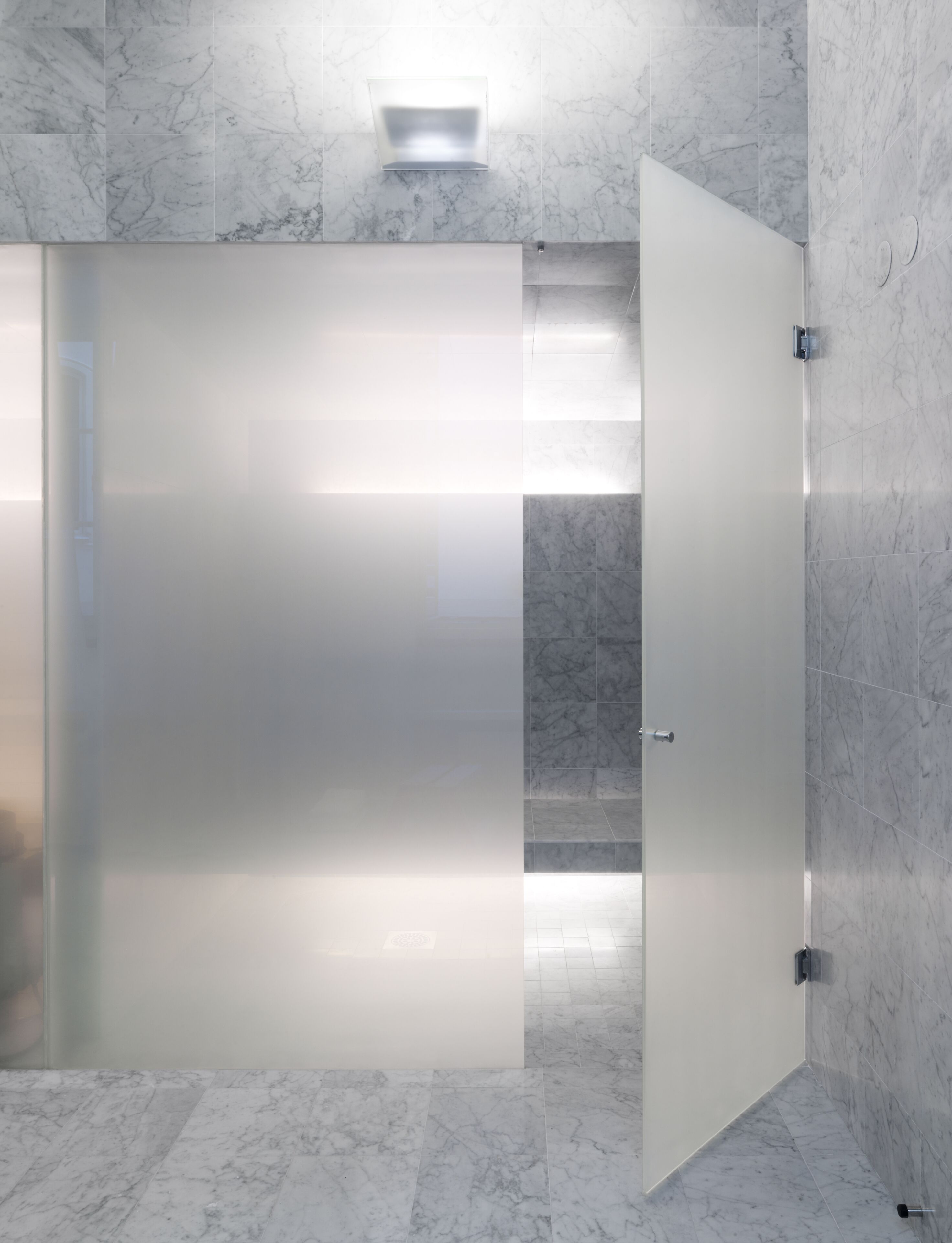 Un baño moderno con una puerta de vidrio satinado, paredes de mármol y suelo de baldosas.
