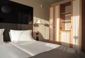 A hotel room with a bed, a nightstand, a lamp, and a wardrobe.