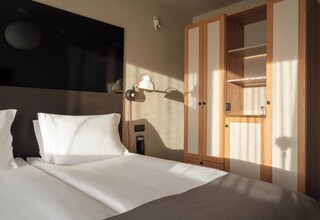 A hotel room with a bed, a nightstand, a lamp, and a wardrobe.