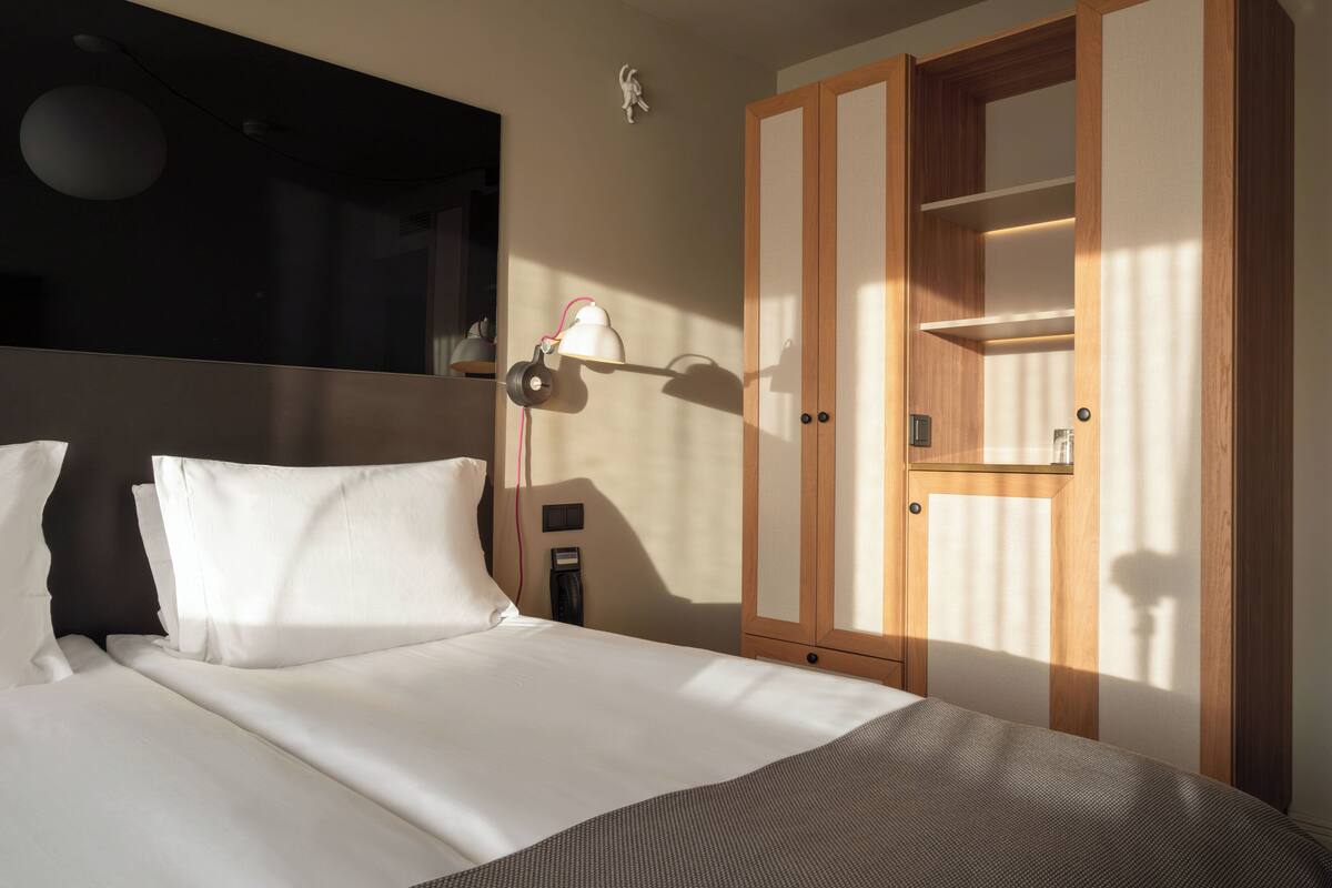 A hotel room with a bed, a nightstand, a lamp, and a wardrobe.