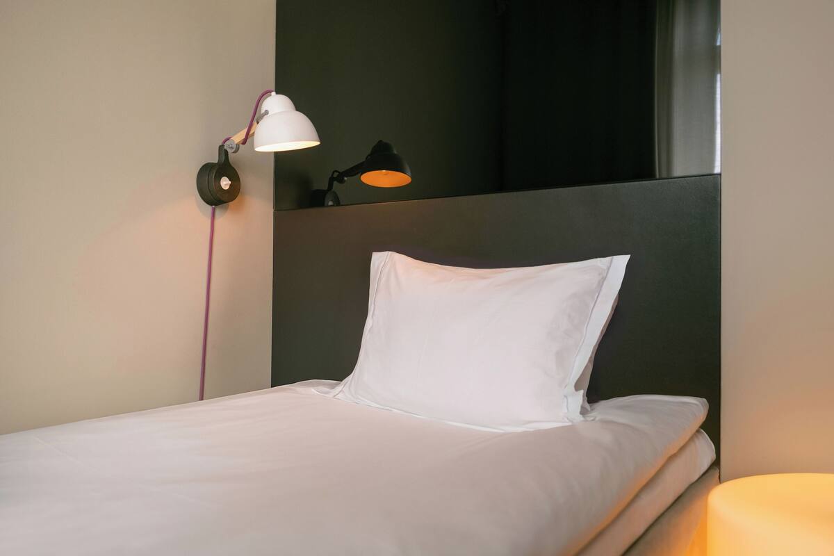 A neatly made bed with white bedding, a black headboard, and two wall-mounted lamps providing light.