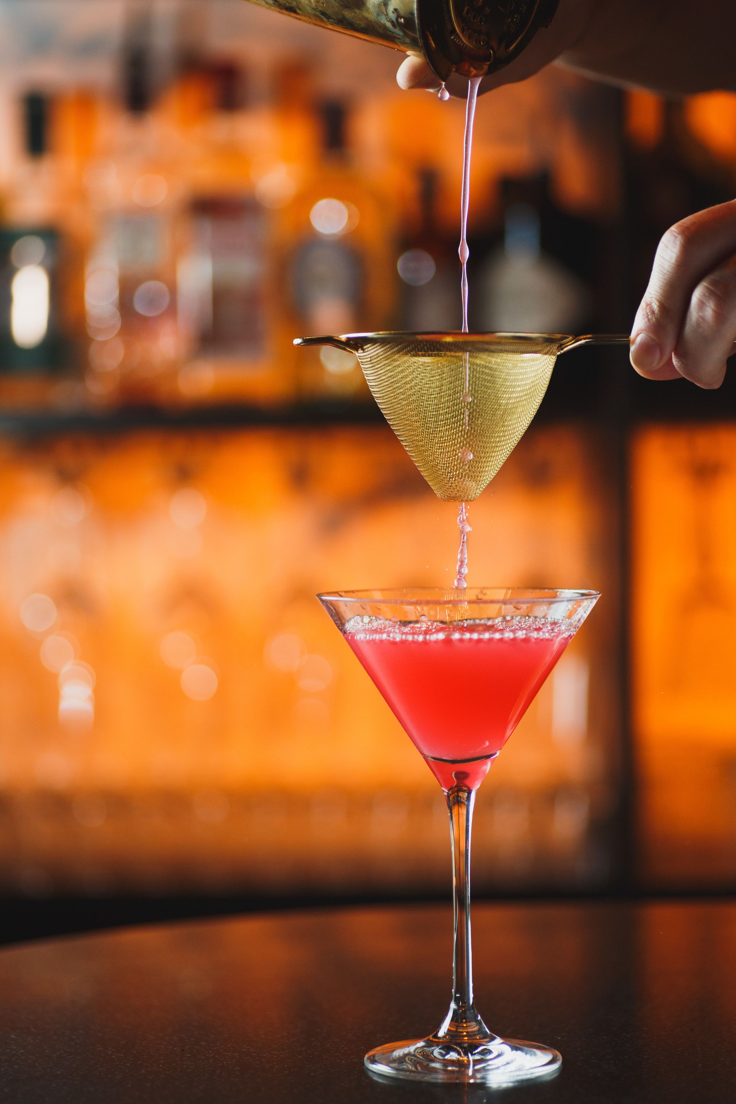 A cocktail being poured into a martini glass.