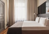 A neatly made bed with white linens, a dark headboard, and a bedside lamp.
